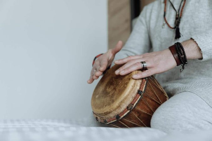 Un percussionniste joue du djembe sur un lit. Gros plan sur les mains sur l'idiophone, la bague et les bracelets.