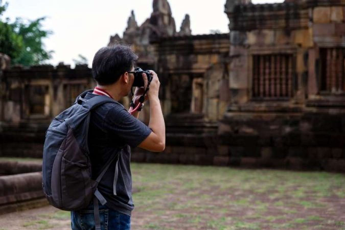 Un homme avec un sac à dos prend des photos de voyage d'un temple ancien en ruine.