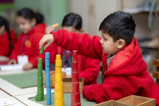 Un jeune garçon manipule des cylindres colorés en classe, illustrant les principes de la méthode Montessori.