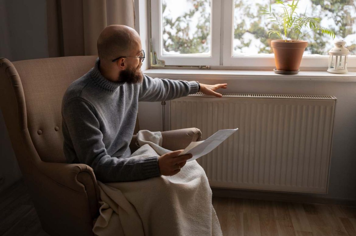 Un homme assis dans un fauteuil évalue un radiateur dans le cadre d'un projet de prêt à taux zéro installation chauffage.